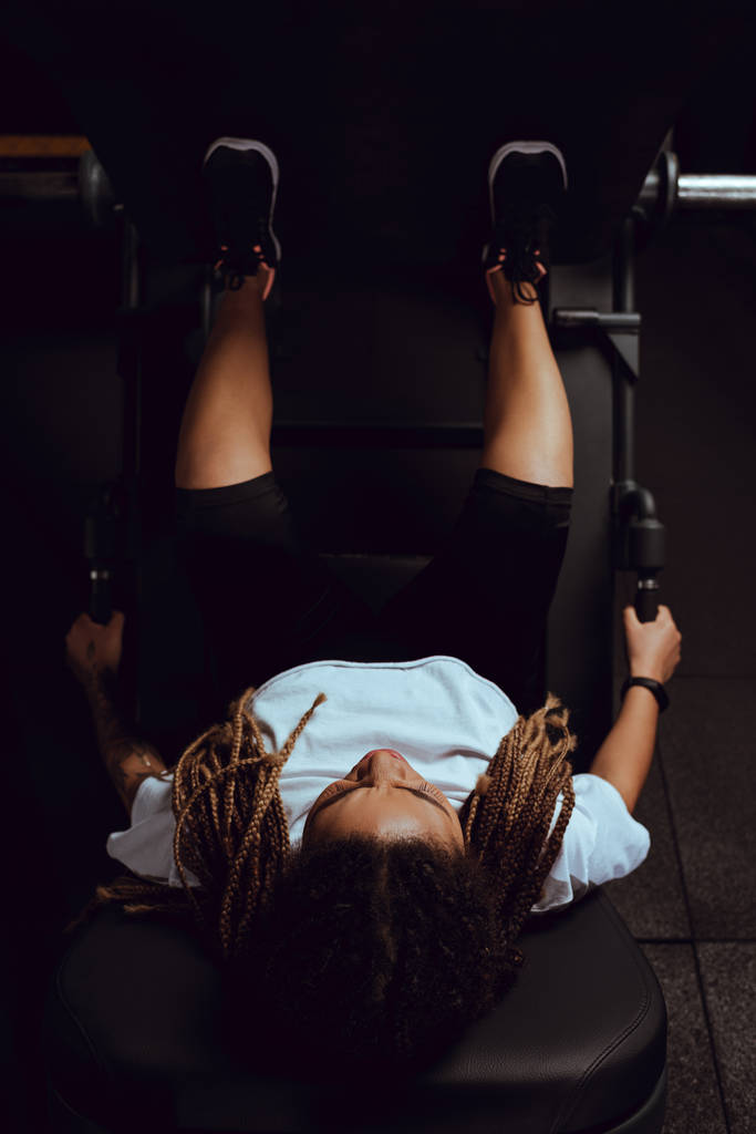 top uitzicht van getatoeëerd Afrikaans Amerikaans meisje uit te werken op fitness apparaat - Foto, afbeelding