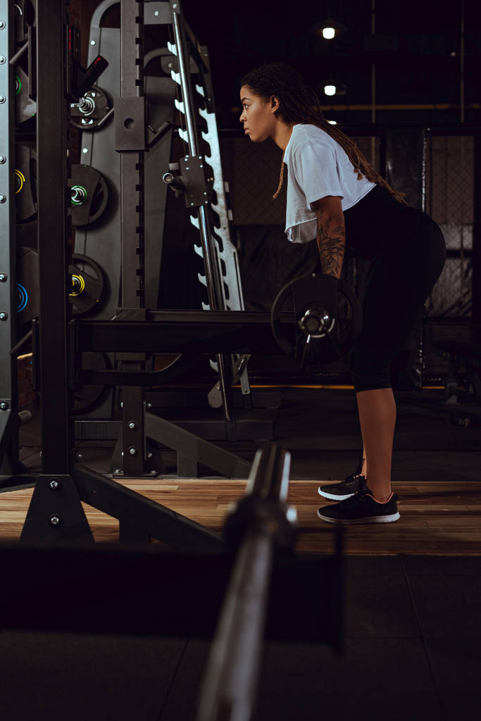 vista lateral de la deportista afroamericana haciendo ejercicio con barra
  - Foto, Imagen