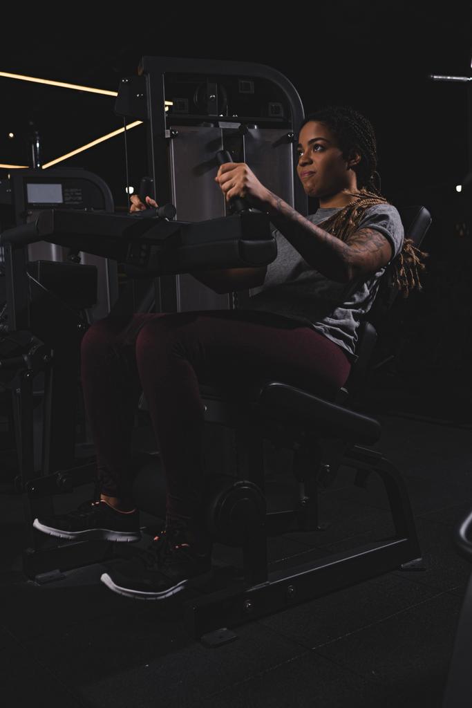 getatoeëerd Afrikaans amerikaans meisje met dreadlocks uit te werken op fitness apparaat - Foto, afbeelding