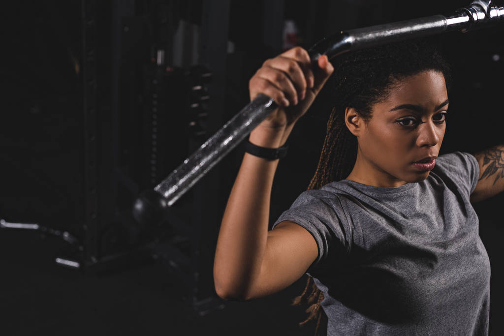επιλεκτική εστίαση της νεαρής αφρικανικής Αμερικής κορίτσι με τατουάζ εκπαίδευση στο μηχάνημα γυμναστικής - Φωτογραφία, εικόνα