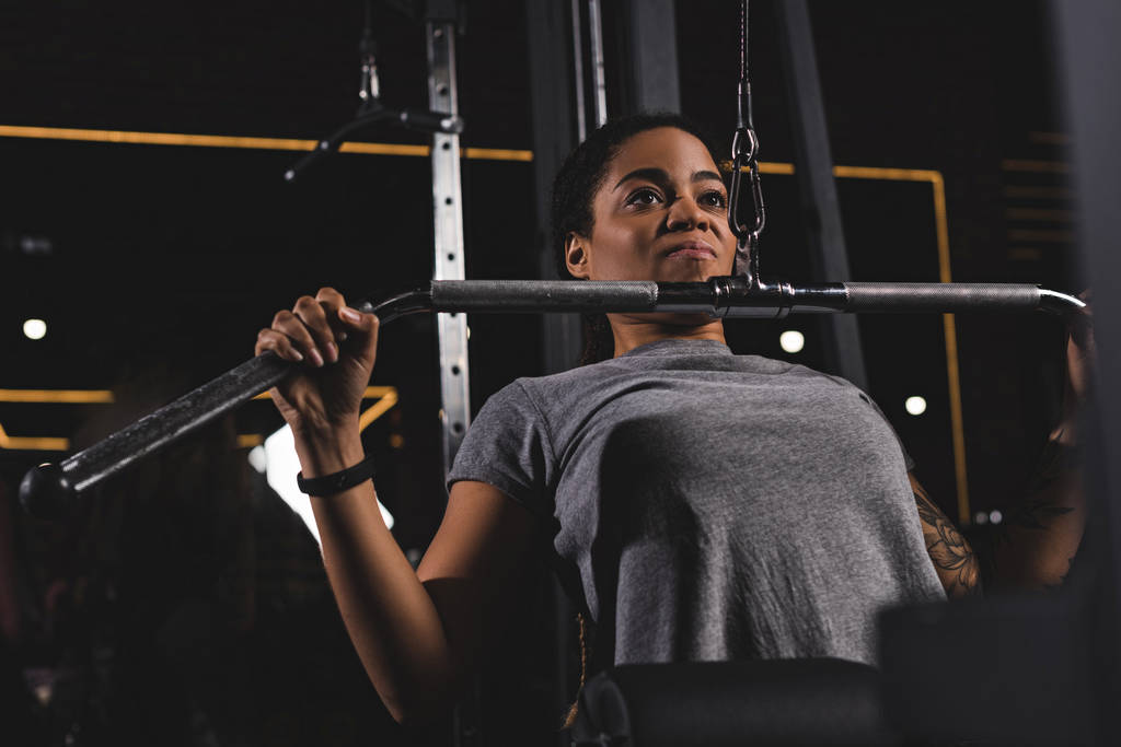 enfoque selectivo de chica afroamericana con entrenamiento de tatuaje en la máquina de fitness en el gimnasio
  - Foto, imagen