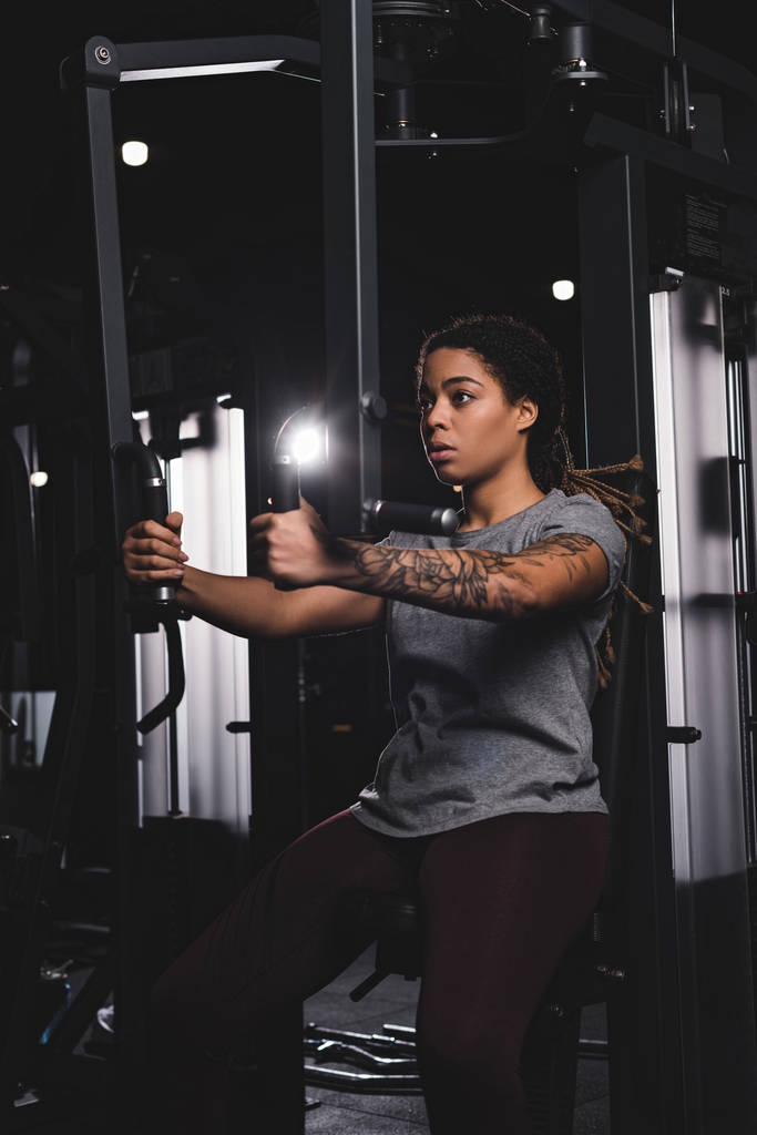 sportive african american girl with tattoo training on gym machine  - Fotoğraf, Görsel