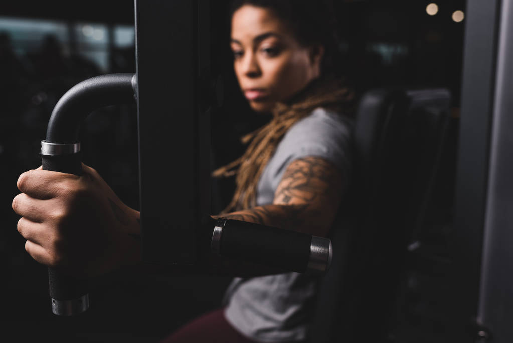 selective focus of attractive african american girl with tattoo exercising on gym machine  - Fotoğraf, Görsel
