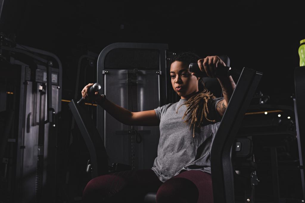 athletic and tattooed african american girl exercising on gym machine  - Photo, Image