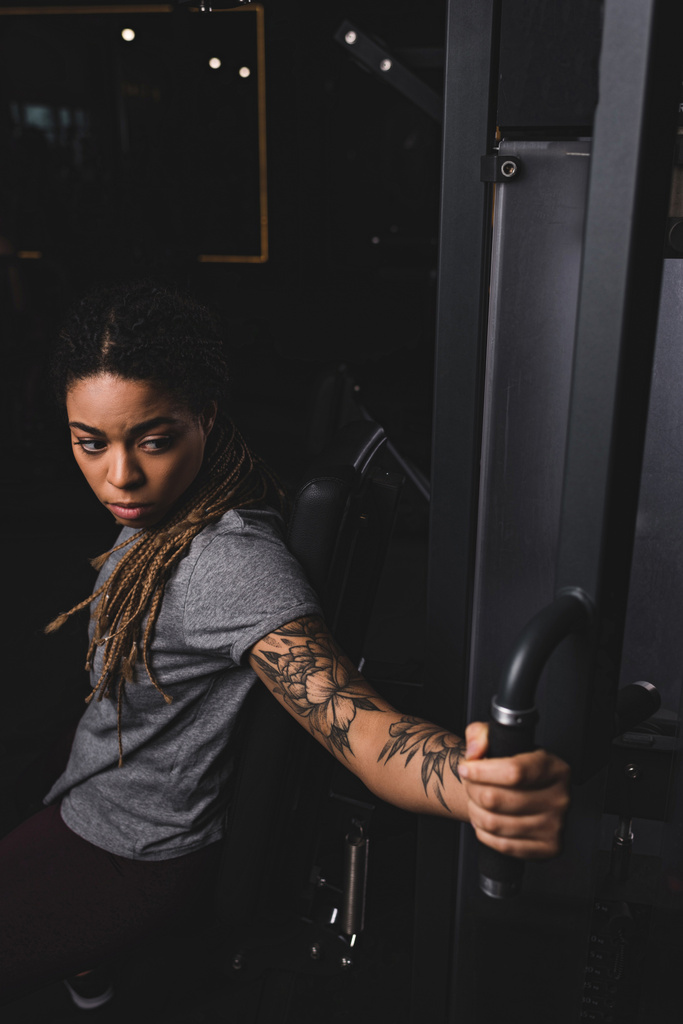 szelektív fókusz atlétikai és tetovált afro-amerikai nő gyakorló tornaterem gép  - Fotó, kép