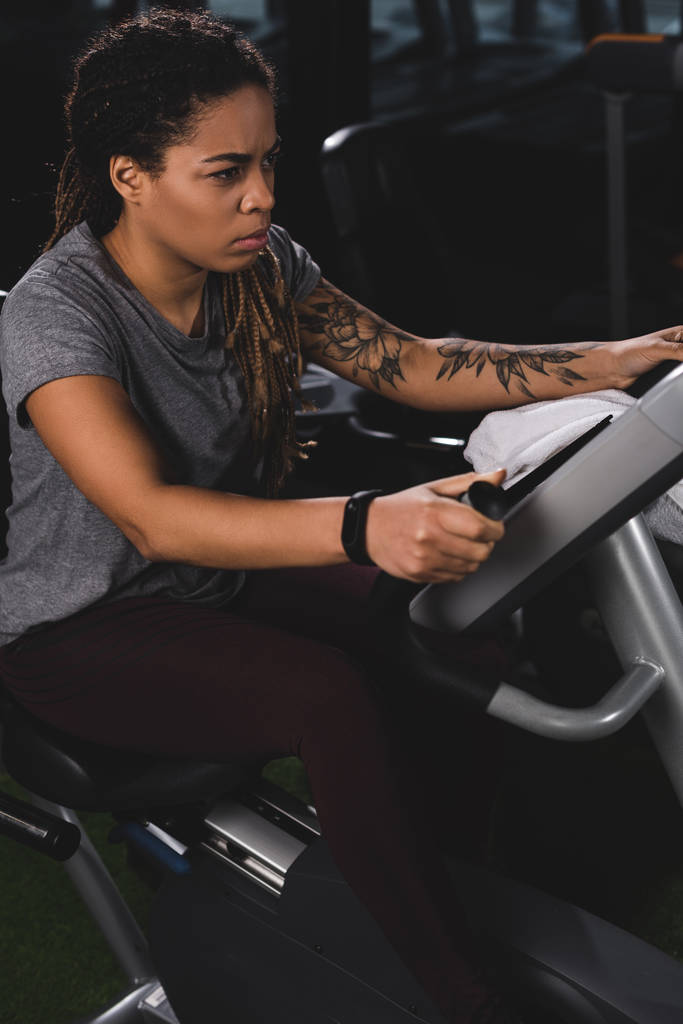 gericht Afrikaans amerikaans meisje met tatoeage training op sportschool machine  - Foto, afbeelding