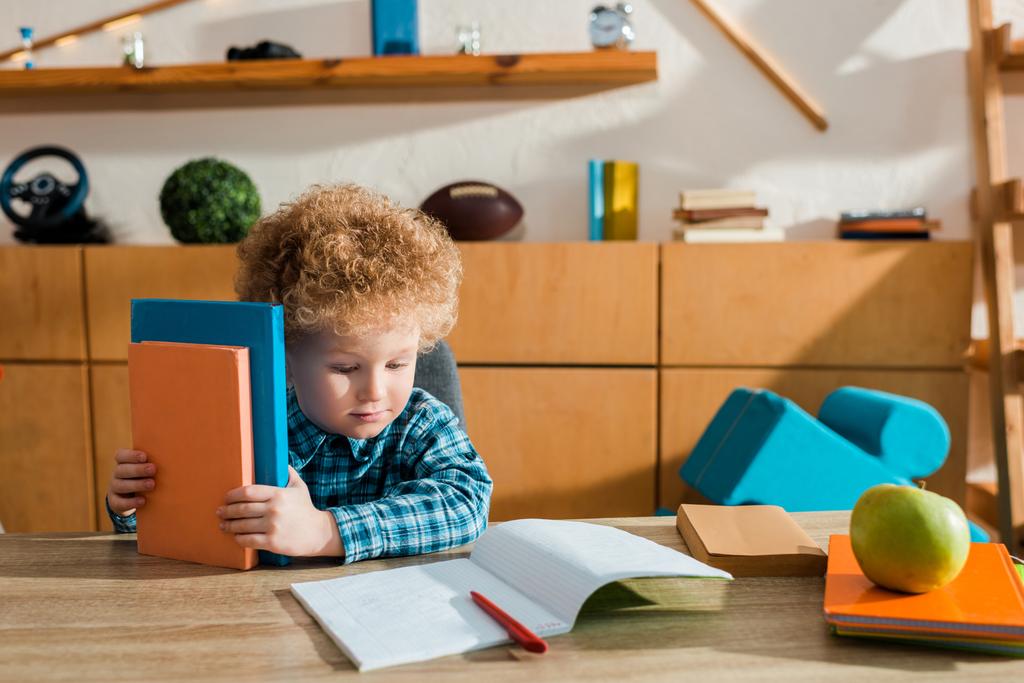 słodkie inteligentne dziecko patrząc na notatnik i trzymając książki  - Zdjęcie, obraz