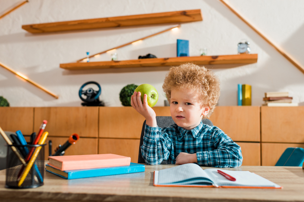 χαριτωμένο έξυπνο παιδί κρατώντας ώριμο μήλο και κοιτάζοντας την κάμερα  - Φωτογραφία, εικόνα