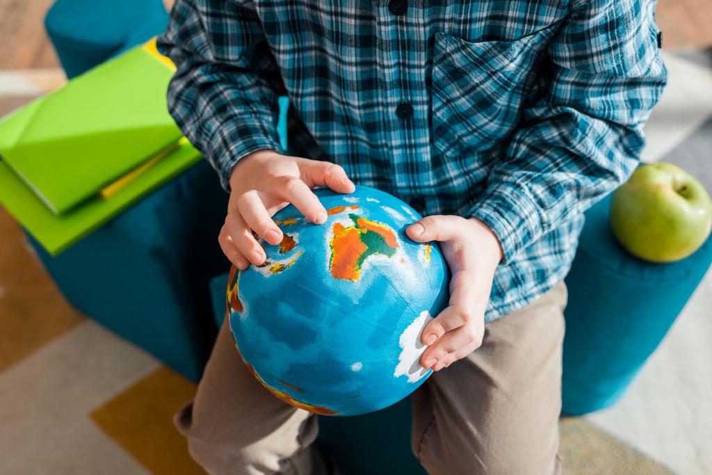 bijgesneden beeld van slimme kind houden wereldbol terwijl zitten thuis - Foto, afbeelding