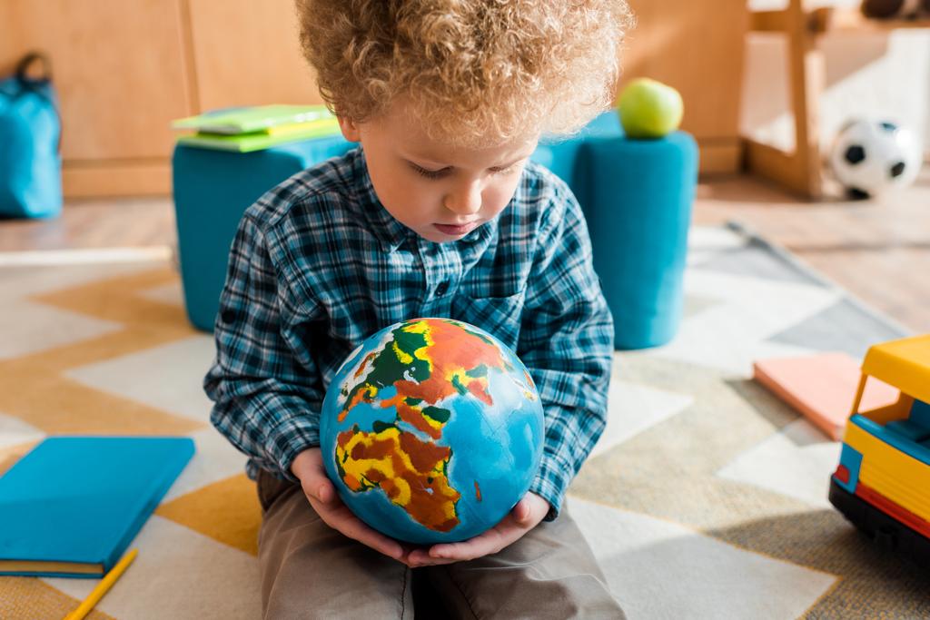 intelligentes Kind blickt auf Globus, während es auf Teppich sitzt  - Foto, Bild