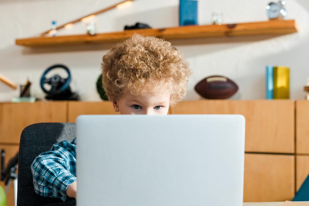 επιλεκτική εστίαση του έξυπνου και σγουρού παιδιού χρησιμοποιώντας φορητό υπολογιστή  - Φωτογραφία, εικόνα
