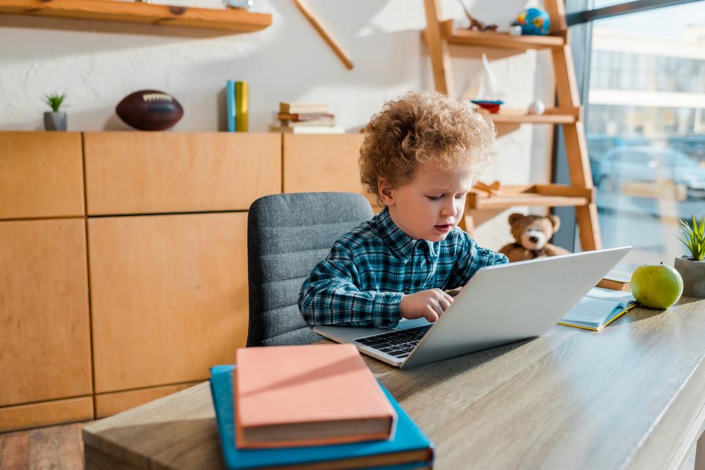 selectieve focus van krullend kind typen op laptop in de buurt van boeken  - Foto, afbeelding