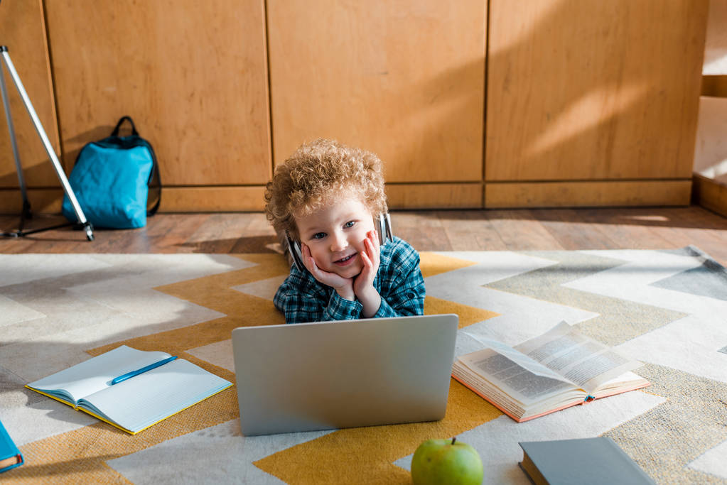 gelukkig kind in koptelefoon liggend op de vloer in de buurt van laptop  - Foto, afbeelding