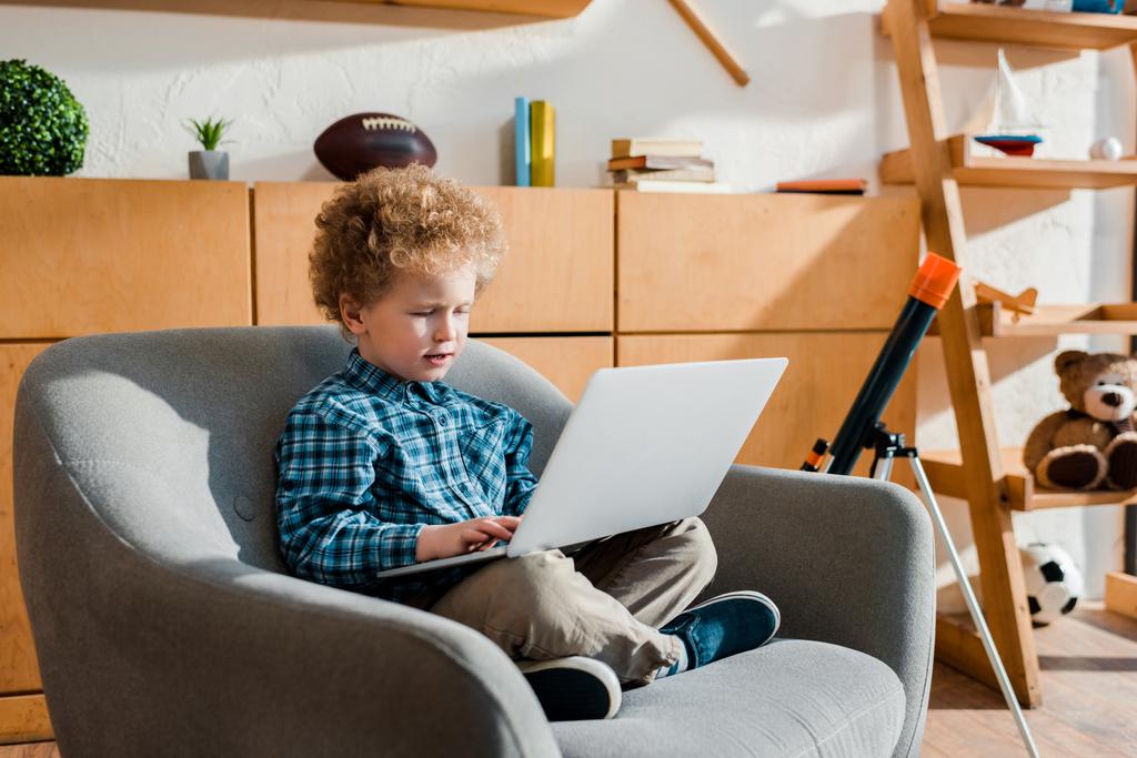 söpö lapsi istuu nojatuolissa ja käyttää kannettavaa tietokonetta
  - Valokuva, kuva