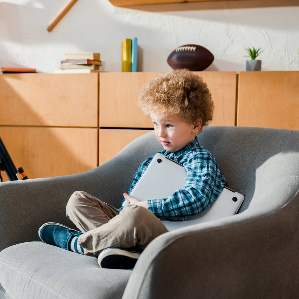 niño inteligente sentado en sillón con portátil
  - Foto, Imagen