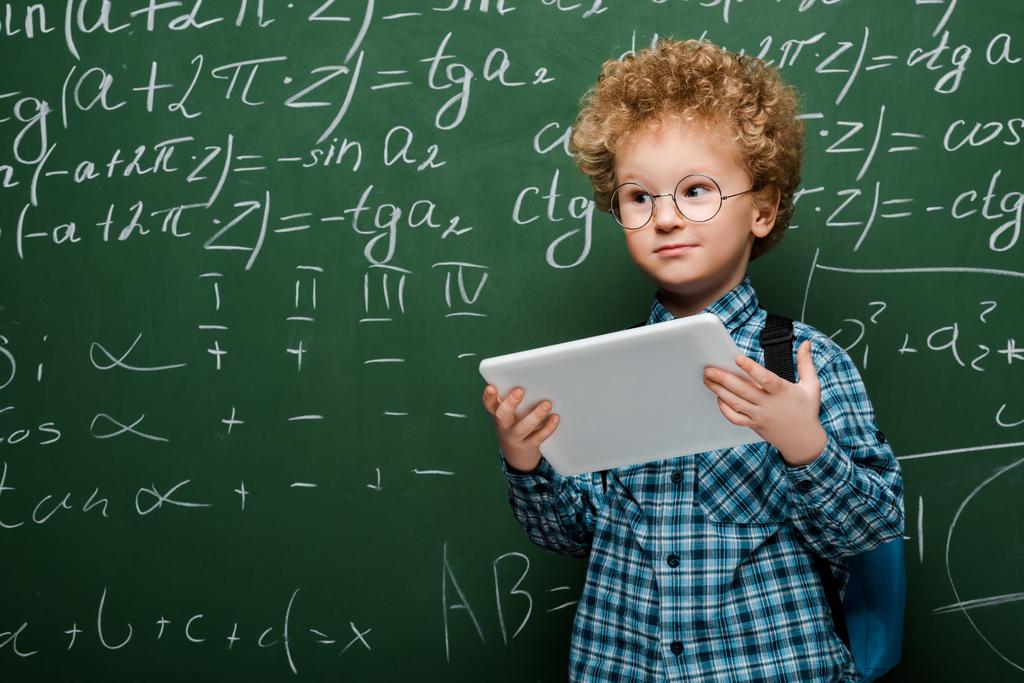 chytré dítě v brýlích drží digitální tablet v blízkosti desky s matematickými vzorci  - Fotografie, Obrázek