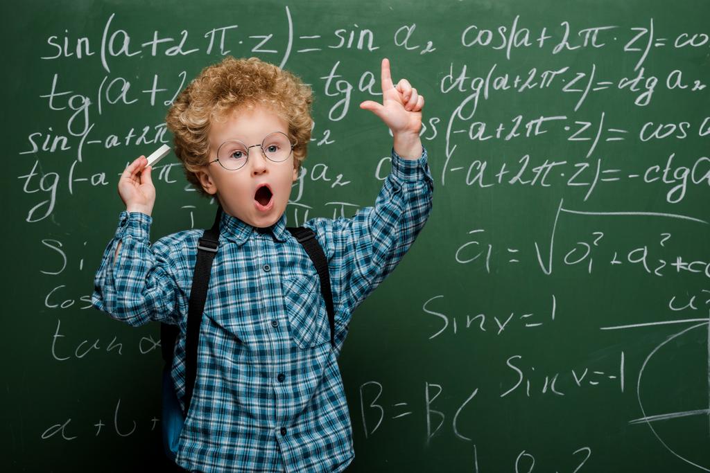 curly kid in glasses gesturing near chalkboard with mathematical formulas  - Photo, Image