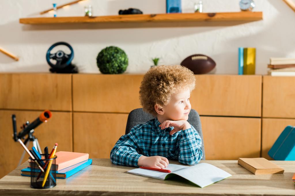 bambino intelligente guardando lontano vicino ai libri sul tavolo
  - Foto, immagini