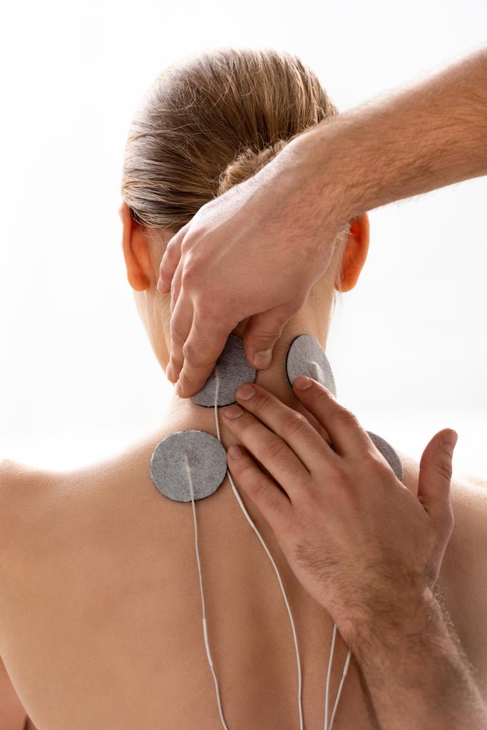Θεραπευτής κρατώντας ηλεκτρόδια διέγερσης στο λαιμό του ασθενούς κατά τη διάρκεια θεραπείας με ηλεκτρόδια που απομονώνονται σε λευκό - Φωτογραφία, εικόνα