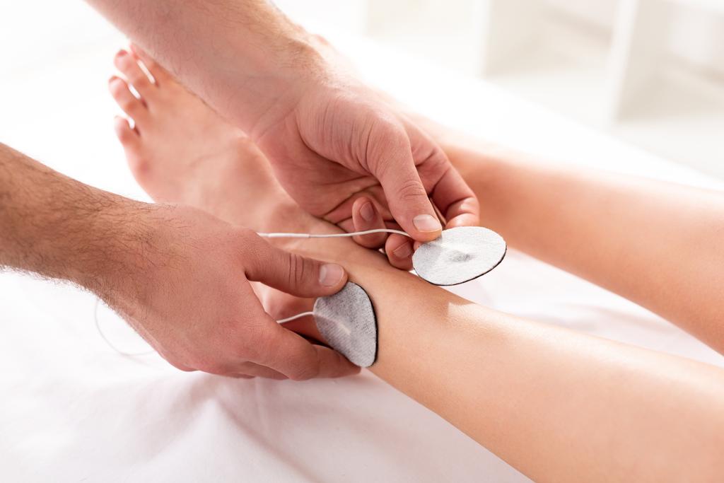 Προβολή των ηλεκτροδίων ρύθμισης θεραπευτή στο πόδι του ασθενούς κατά τη διάρκεια της ηλεκτροθεραπείας στην κλινική - Φωτογραφία, εικόνα