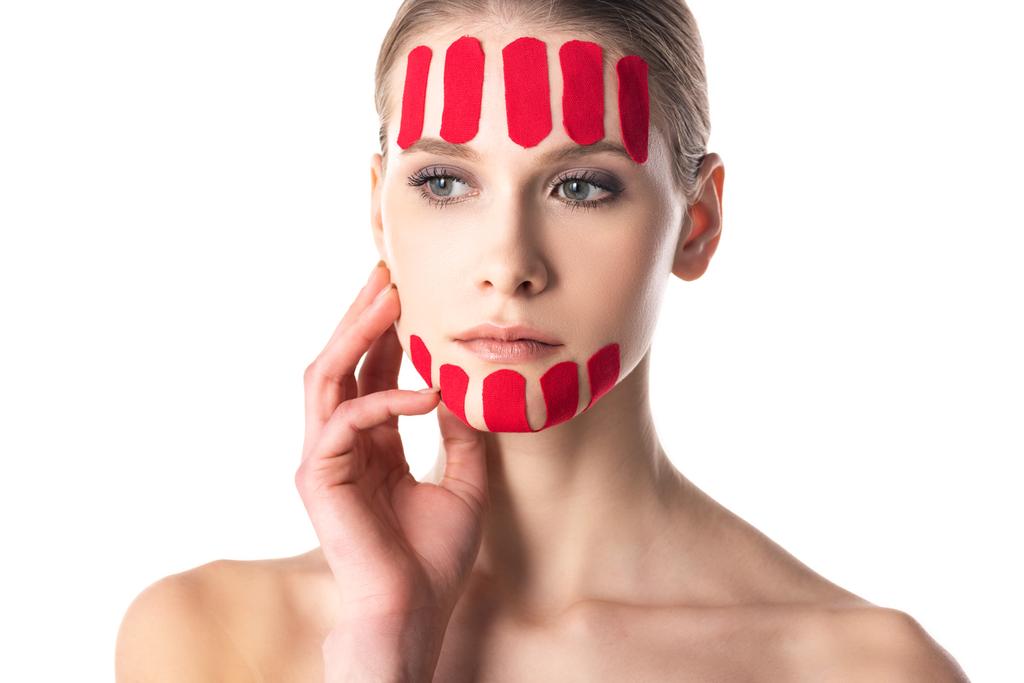Молодая женщина с кинезиологическими кассетами на лице смотрит в сторону изолированной на белом
 - Фото, изображение