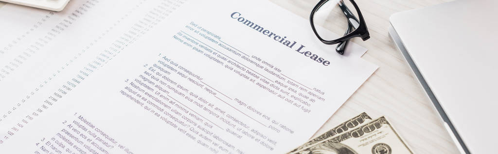 panoramische opname van documenten met commerciële lease belettering in de buurt van geld en bril op het bureau  - Foto, afbeelding