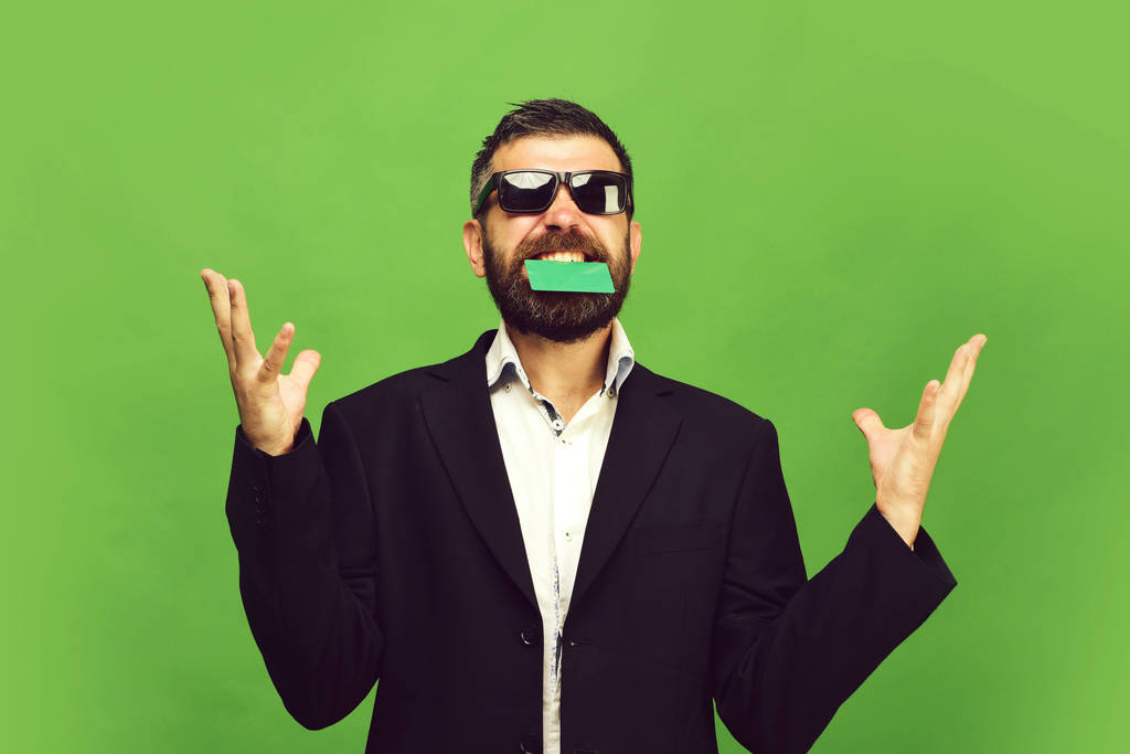 Человек с темной бородой держит зеленую визитку в зубах
 - Фото, изображение