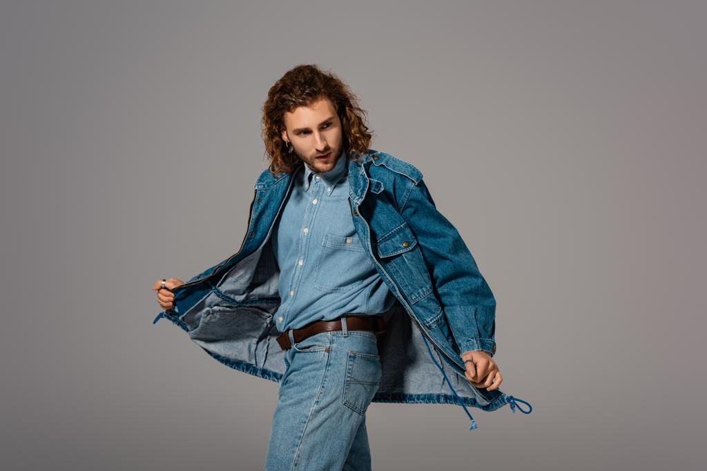 gutaussehender und stilvoller Mann in Jeansjacke und Jeans, der isoliert von grau wegschaut - Foto, Bild