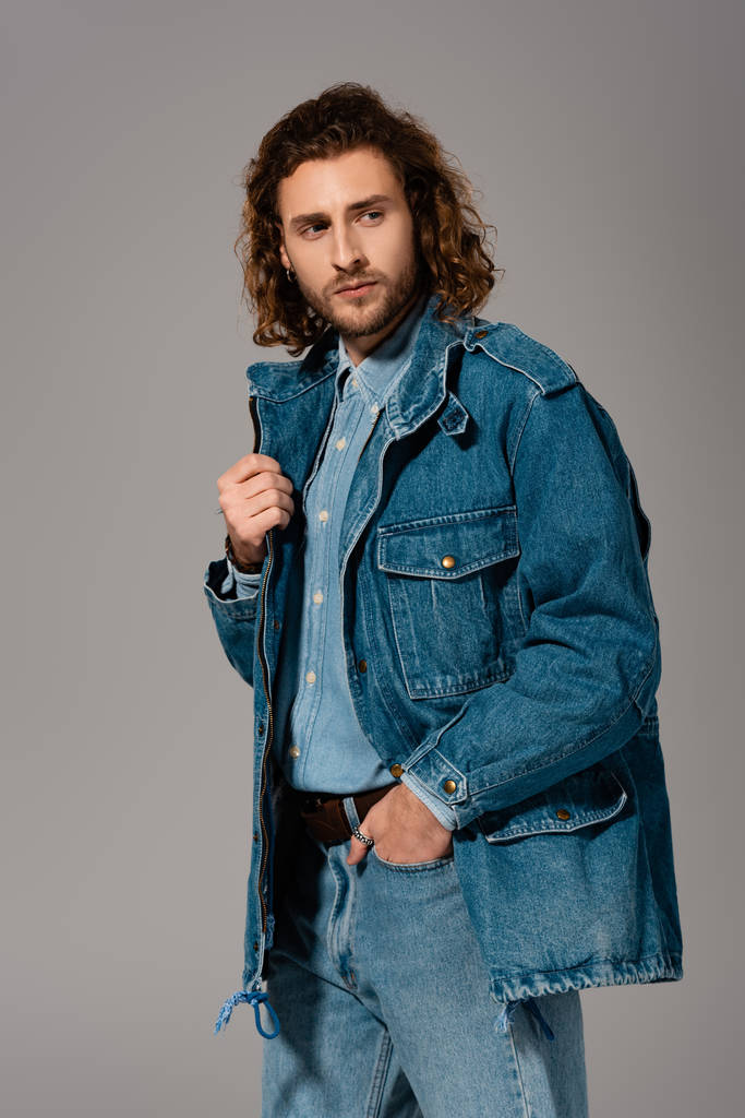 schöner und stilvoller Mann in Jeansjacke mit Hand in Tasche isoliert auf grau - Foto, Bild