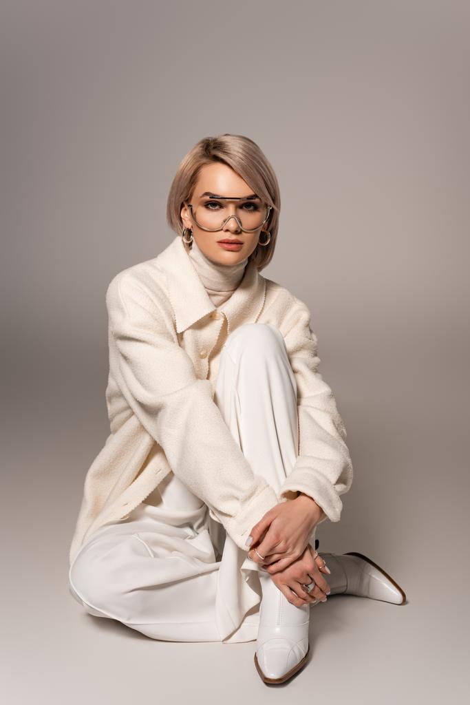 attractive woman in white coat and trousers looking at camera on grey background  - Photo, Image