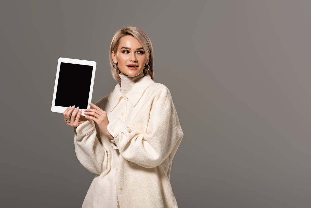 atrakcyjna i uśmiechnięta kobieta w białym płaszczu z cyfrową tabletką odizolowaną na szaro  - Zdjęcie, obraz