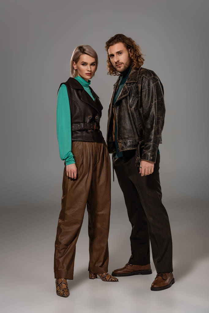 woman in vest and man in leather jacket looking at camera on grey background  - Photo, Image