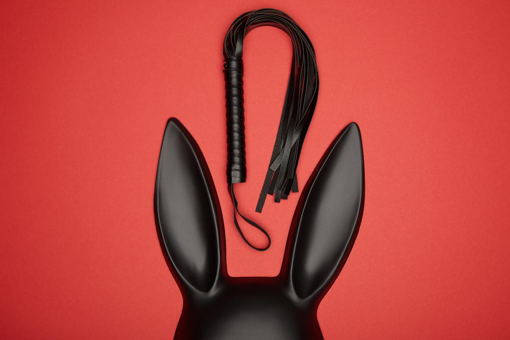 Kırmızı renkte siyah tavşan maskesi ve kırbaç. - Fotoğraf, Görsel
