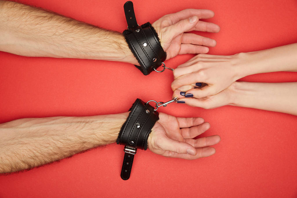 cropped view of woman holding handcuffs on man isolated on red - Photo, Image