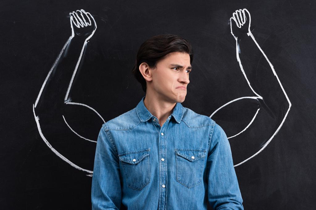 emotional young man with strong muscular arms drawing on blackboard - Fotoğraf, Görsel