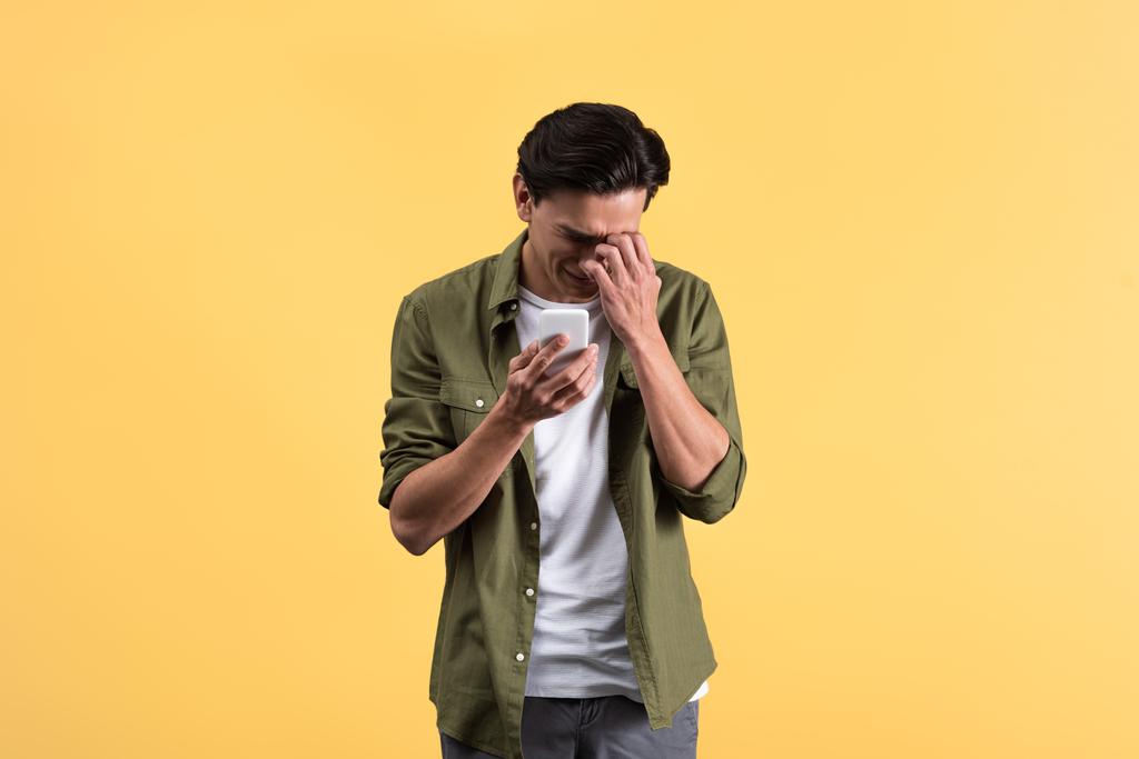 emotional crying young man using smartphone, isolated on yellow - Photo, Image