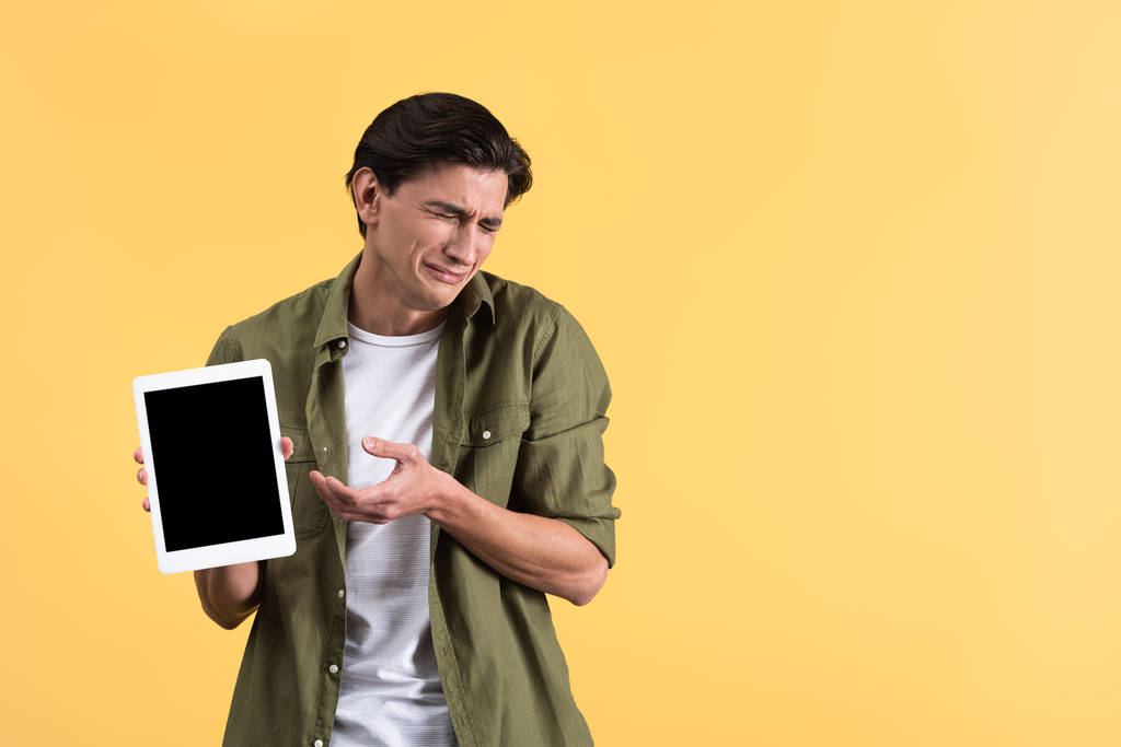 trauriger weinender Mann zeigt digitales Tablet mit leerem Bildschirm, isoliert auf gelb - Foto, Bild