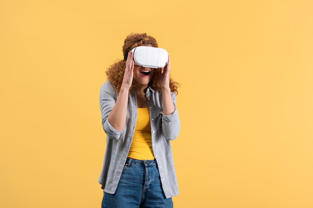 aufgeregtes rothaariges Mädchen mit Virtual Reality Headset, isoliert auf gelb - Foto, Bild