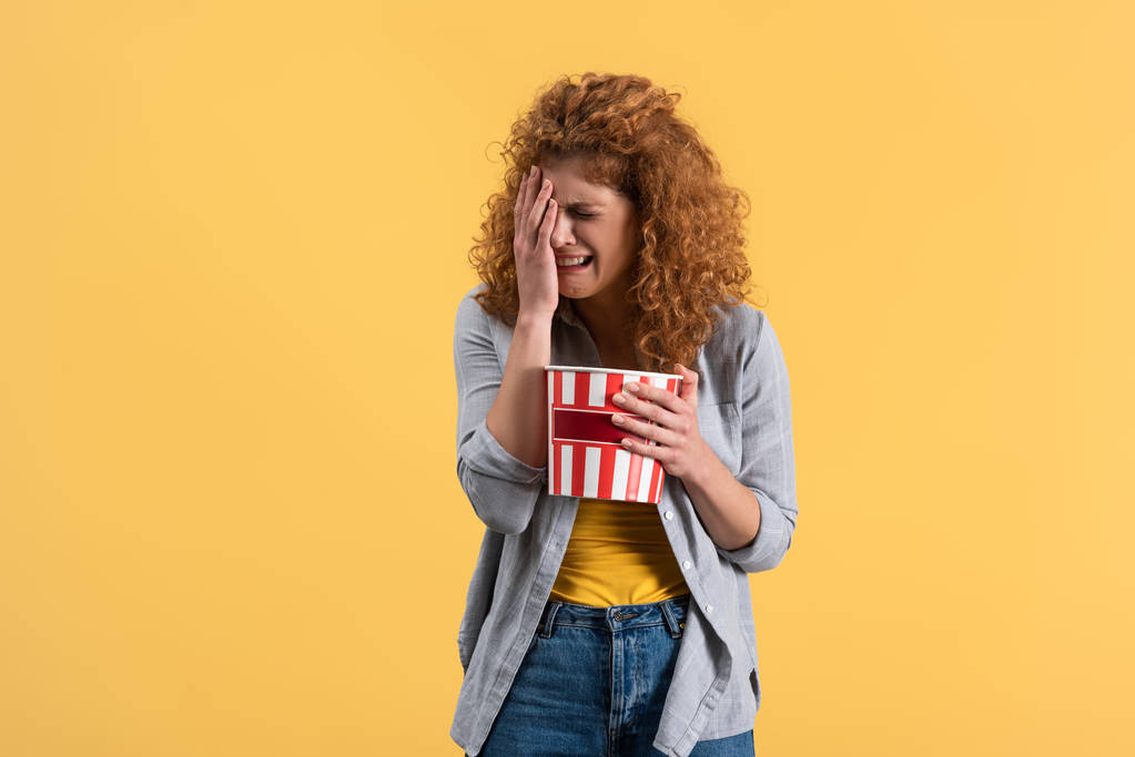 rozčilená dívka pláče a sleduje film s kbelíkem popcornu, izolované na žluté  - Fotografie, Obrázek