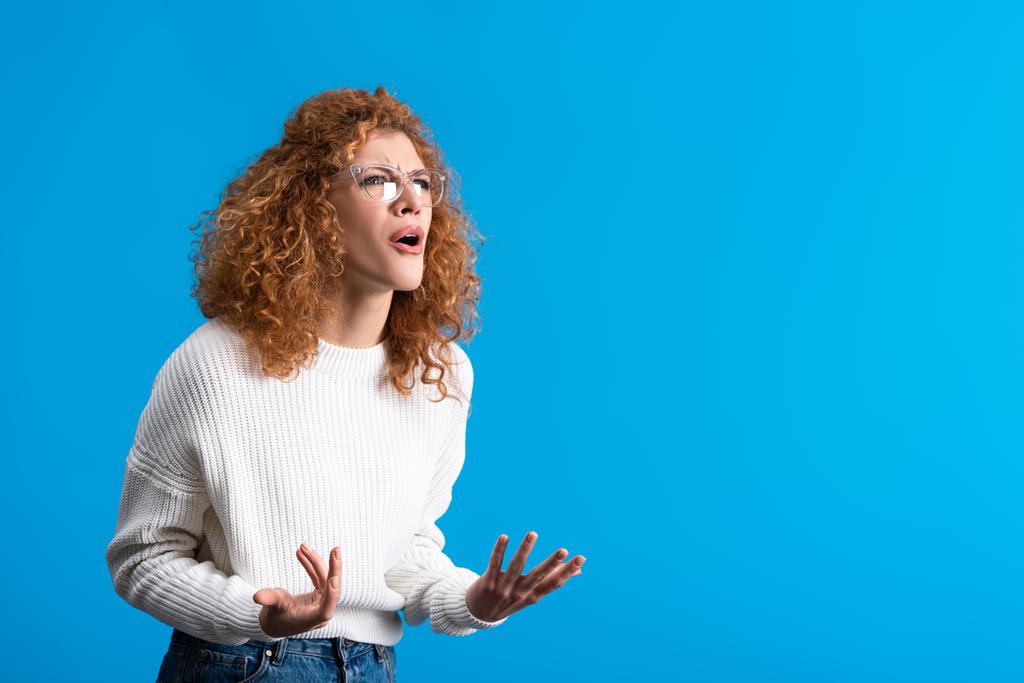 aggressive yelling redhead girl in eyeglasses, isolated on blue - Photo, Image
