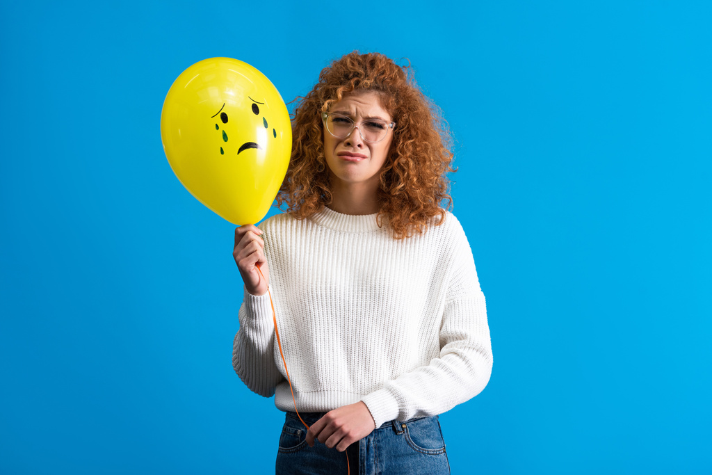 upset girl holding yellow balloon with crying face, isolated on blue - 写真・画像