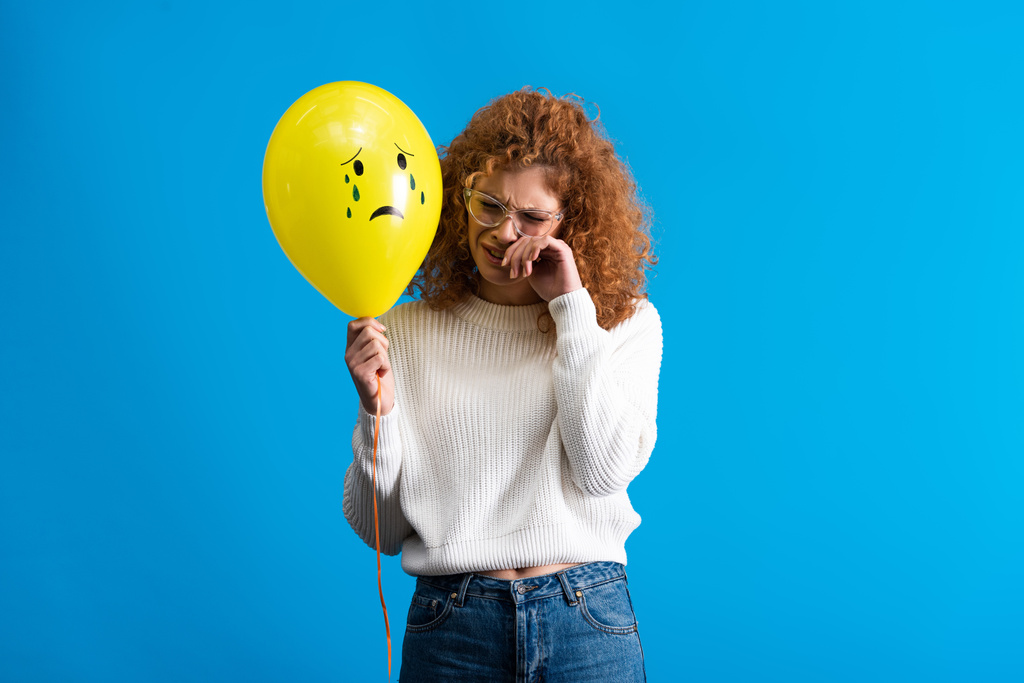 solitaire rousse fille tenant ballon jaune avec visage triste, isolé sur bleu
 - Photo, image