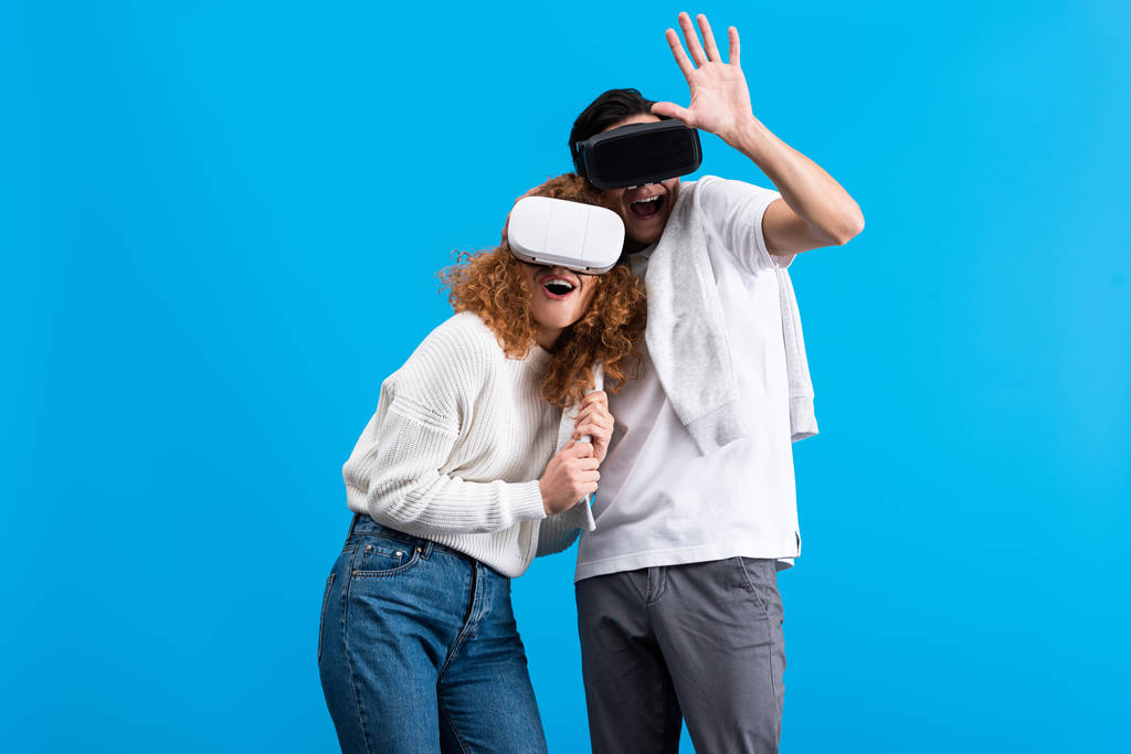 pareja excitada usando auriculares de realidad virtual, aislados en azul
 - Foto, imagen
