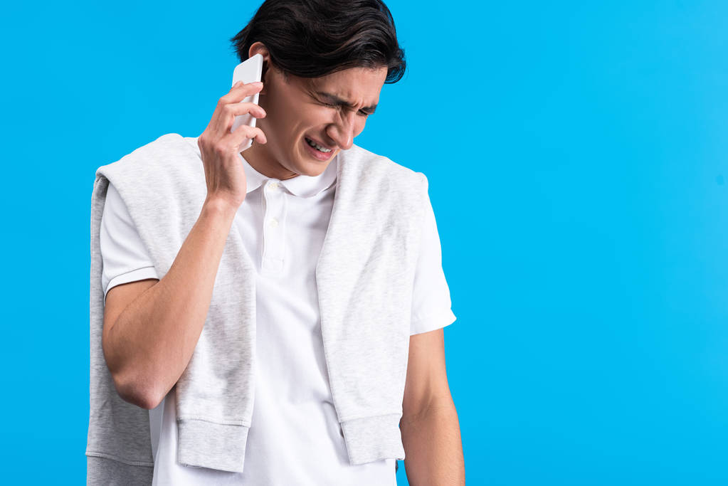 stresovaný mladý muž mluví na smartphonu, izolovaný na modré - Fotografie, Obrázek