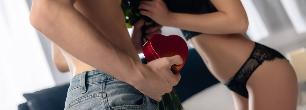 tiro panorâmico de namorado dando buquê e caixa em forma de coração para namorada sexy em 14 de fevereiro
 - Foto, Imagem