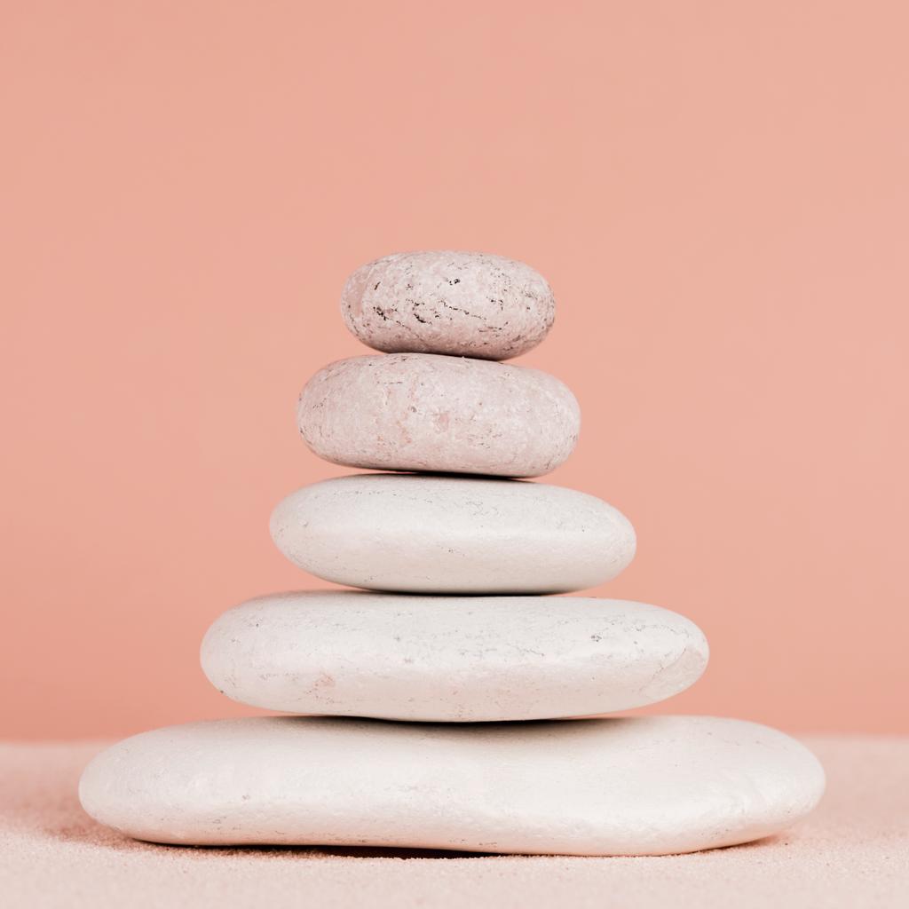 Close up view of stacked zen stones on sand isolated on peach  - Photo, Image