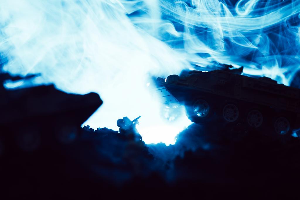 Speelgoedtanks en soldaat met blauwe rook op zwarte achtergrond, battle scene - Foto, afbeelding