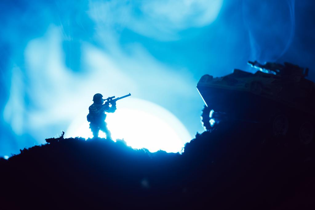 Escena de batalla con guerrero de juguete y tanque con luna y humo al fondo
 - Foto, Imagen
