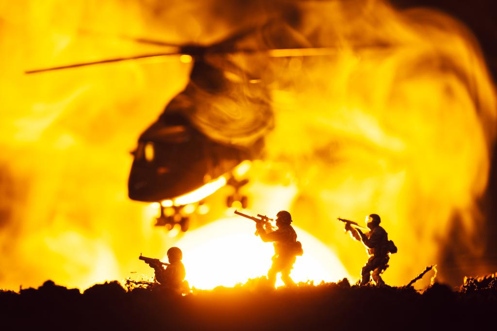 Cena de batalha com guerreiros de brinquedo e helicóptero em fumaça com o pôr do sol no fundo
 - Foto, Imagem