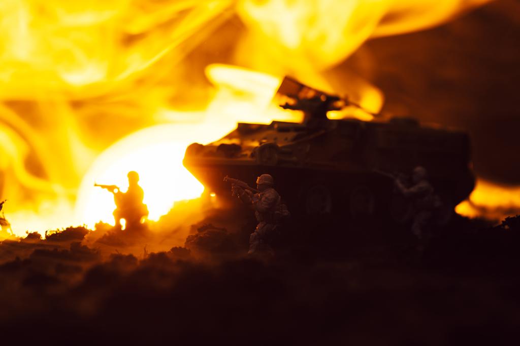 Speelgoed soldaten met tank, vuur en zonsondergang op zwarte achtergrond, battle scene - Foto, afbeelding